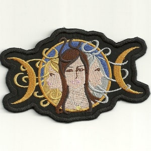 May include: Embroidered patch featuring a triple moon symbol with a woman's face in the centre. The moon is gold and the woman's face is surrounded by a blue circle.