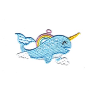 May include: A blue embroidered narwhal with a rainbow on its back and a yellow horn. The narwhal is surrounded by white clouds.