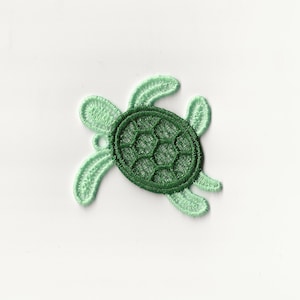 Op de afbeelding: Een groene en lichtgroene geborduurde schildpad-applicatie. De schildpad heeft een gedetailleerde schild en is perfect om een ​​toets van whimsy toe te voegen aan knutselwerk.