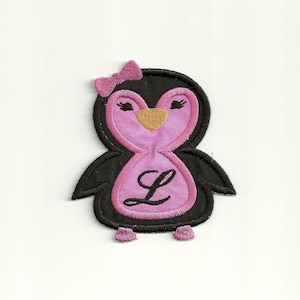May include: Embroidered iron-on patch of a pink penguin with a black bow, black eyes, and a gold beak. The penguin has the letter "L" on its chest.