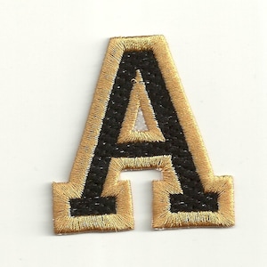 以下が含まれることがあります： 金色の縁取りが付いた黒いフェルトの文字A。文字は刺繍されており、ビンテージな外観です。