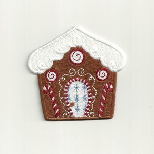 Op de afbeelding: Een bruin peperkoekhuis met witte glazuur en rode en witte snoepstokken. Het huis heeft een blauwe en witte deur met een sneeuwvlokkenpatroon.