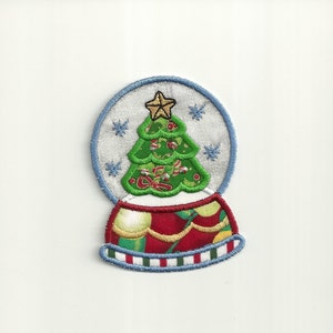 May include: Embroidered Christmas snow globe patch featuring a green Christmas tree with red and white accents, topped with a gold star. The globe has a silver background with blue snowflakes and a blue border. The base is red with green and gold details.