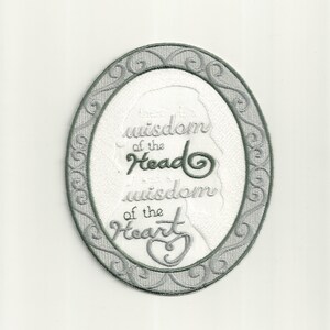 Pode incluir: Patch bordado em forma oval com uma borda decorativa cinza. O patch apresenta o texto "There is wisdom of the Head, there is wisdom of the Heart" em escrita cinza, com uma silhueta de perfil feminino.