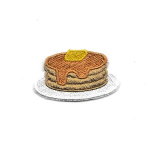 May include: A white plate with a stack of three brown pancakes topped with a yellow pat of butter and brown syrup.