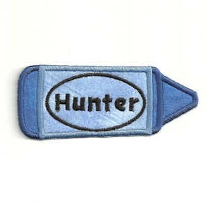 Puede incluir: Parche de denim azul para planchar con un óvalo blanco y el nombre "Hunter" bordado en negro.