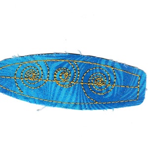 Pode incluir: Uma prancha de surf de tecido azul com redemoinhos bordados em ouro.