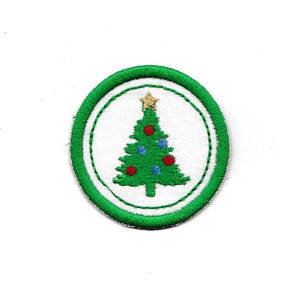 May include: A green embroidered Christmas tree patch with a gold star on top and red and blue ornaments. The patch is surrounded by a white circle and a green outer circle.