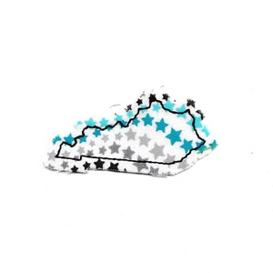 May include: A white fabric patch in the shape of the state of Kentucky with a black outline. The fabric is covered in blue and gray stars.