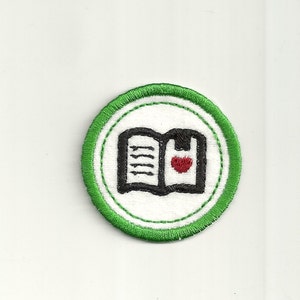 Peut inclure: Écusson brodé vert et blanc avec un livre ouvert noir avec un cœur rouge sur la page de droite. Le livre est entouré d'un cercle vert avec une bordure blanche.