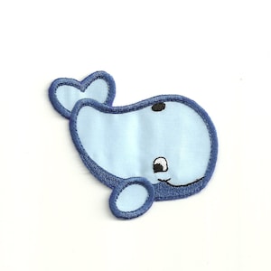 May include: A blue whale applique with a smiling face and a small tail fin. The whale is outlined in dark blue thread.