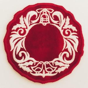 Puede incluir: Un adorno navideño de fieltro rojo con un diseño de corona bordado en blanco. La corona presenta una campana en el centro y intrincados patrones florales.