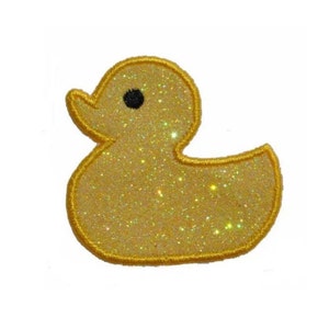 Peut inclure: Un canard en caoutchouc jaune avec un œil noir, fait de tissu pailleté. Le canard est bordé de fil jaune.