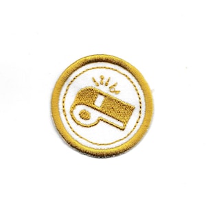 May include: A gold embroidered patch with a white whistle and sound waves. The patch is circular and has a gold border.