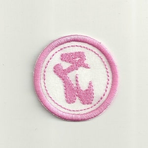 May include: A round, embroidered patch featuring a pink ballet shoe design within a white circle. The circle is bordered by a pink stitched edge. The patch is likely for clothing or accessories.