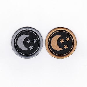 May include: Two embroidered patches with a crescent moon and five-pointed stars. One patch is silver on black fabric with a gray border. The other patch is gold on black fabric with a brown border.