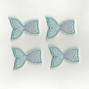 Könnte beinhalten: Vier hellblaue Filz-Meerjungfrauen-Schwanz-Applikationen mit rosa Schuppen. Die Schwänze sind mit einem detaillierten Design bestickt.
