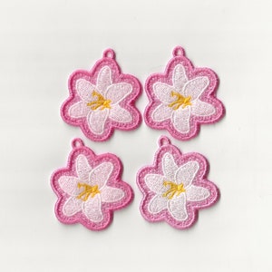 Könnte beinhalten: Vier rosa bestickte Blumenverzierungen mit weißen Zentren und gelben Akzenten. Die Blumen haben die Form eines fünfzackigen Sterns.