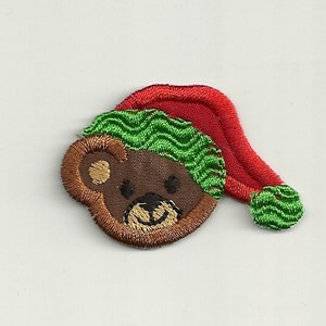 Op de afbeelding: Geborduurde strijk-patch van een bruine beer met een rode en groene kerstmanmuts.