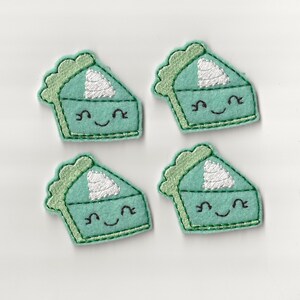 May include: Four green felt patches shaped like a slice of pie with white whipped cream and a smiling face embroidered on each.