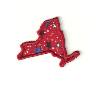 May include: Red felt outline of the state of New York with a white background and a pattern of white, blue, and black stars.