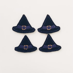 May include: Four black felt witch hats with purple trim and gold buckles. The hats are arranged in two rows of two.