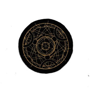 May include: A round, black patch with an intricate gold embroidered design. The design features geometric shapes, lines, and circles, creating a complex pattern. The patch is likely for decorative purposes, such as on clothing or bags.