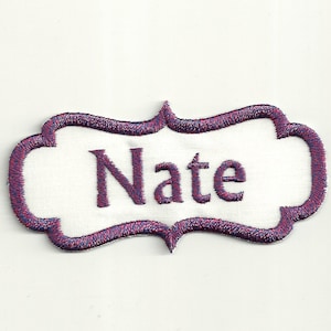 Könnte beinhalten: Weißer bestickter Namensschild mit einem violetten und roten Rand. Der Name "Nate" ist in Lila auf dem Schild gestickt.