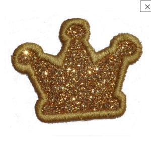 Puede incluir: Una corona dorada con purpurina y un contorno cosido. La corona es un adorno decorativo para manualidades y ropa.