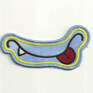 May include: A blue and yellow embroidered patch with a cartoon mouth with a red tongue sticking out.
