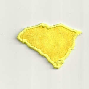 May include: A yellow felt outline of the state of South Carolina. The outline is stitched with a yellow thread.