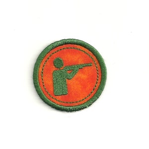 May include: Green and orange embroidered patch with a silhouette of a person holding a rifle.