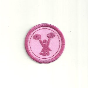 Puede incluir: Parche bordado rosa con una silueta de animadora sosteniendo pompones.