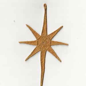 Può includere: Un ornamento dorato a forma di stella con una lunga coda appuntita. La stella ha otto punte ed è realizzata in un materiale intrecciato.