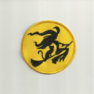May include: A yellow embroidered patch with a black silhouette of a witch flying on a broomstick with a black cat.