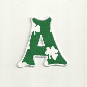 May include: Green felt letter A with white shamrock pattern and white stitching around the edges.