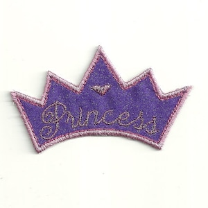 Puede incluir: Corona de fieltro morado con costuras rosas y la palabra "Princesa" bordada en hilo de purpurina plateado.