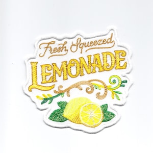 Może przedstawiać: Naszywka haftowana do prasowania z białym tłem i żółtym napisem "Fresh Squeezed Lemonade". Napis jest otoczony zielonym, liściastym winoroślą z żółtym cytryną.