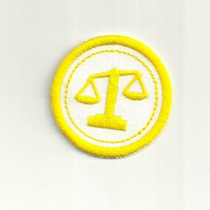 May include: A yellow embroidered patch with a white background featuring a yellow scale of justice design.
