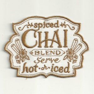 Op de afbeelding: Een gouden geborduurde patch met de tekst "Spiced Chai Blend Serve hot or iced".