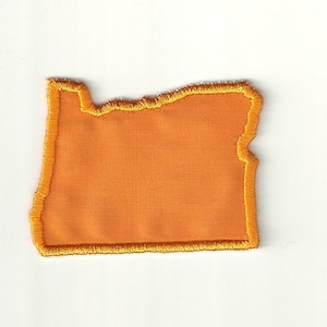 Puede incluir: Contorno de fieltro naranja del estado de Oregón, con un borde cosido amarillo.