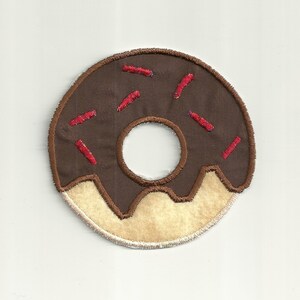 May include: A brown chocolate donut with red sprinkles. The donut has a white frosting ring around the hole.