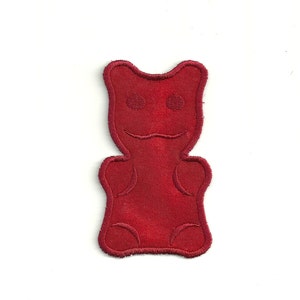 Könnte beinhalten: Ein roter Gummibärchen-Patch mit einem lächelnden Gesicht.