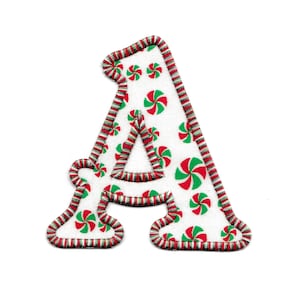 May include: A white fabric letter A with a red and green candy cane pattern. The letter is outlined in red and green thread.