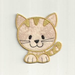 May include: A light pink felt cat applique with gold embroidered details. The cat has a smiling face with black eyes and a striped tail.