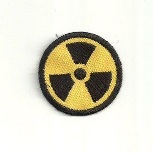 Pode incluir: Um remendo bordado amarelo e preto com um símbolo de radiação.