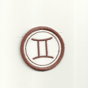 Puede incluir: Parche bordado marrón con el signo del zodíaco Géminis, sobre fondo blanco y con un círculo exterior marrón.