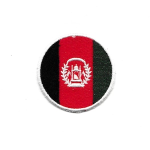 May include: A circular patch featuring the flag of Afghanistan. The design includes vertical stripes of black, red, and green. The red stripe contains a white emblem. The patch has a white border.