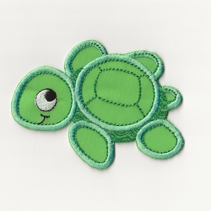 May include: Green felt applique of a cartoon turtle with a smiling face and one large eye. The turtle has a green shell with a stitched pattern.