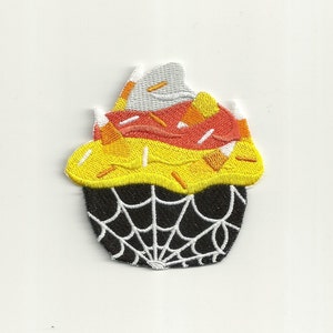 May include: A black and white spiderweb cupcake with yellow, orange, and white frosting and candy corn sprinkles.